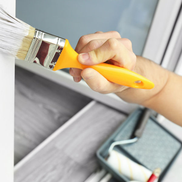 Painter brushes fresh paint over the trim around a window